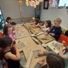 Kindergeburtstagsgesellschaft sitzt gemeinsam am Werktisch beim Töpfer-Kindergeburtstag im MainKreativRaum